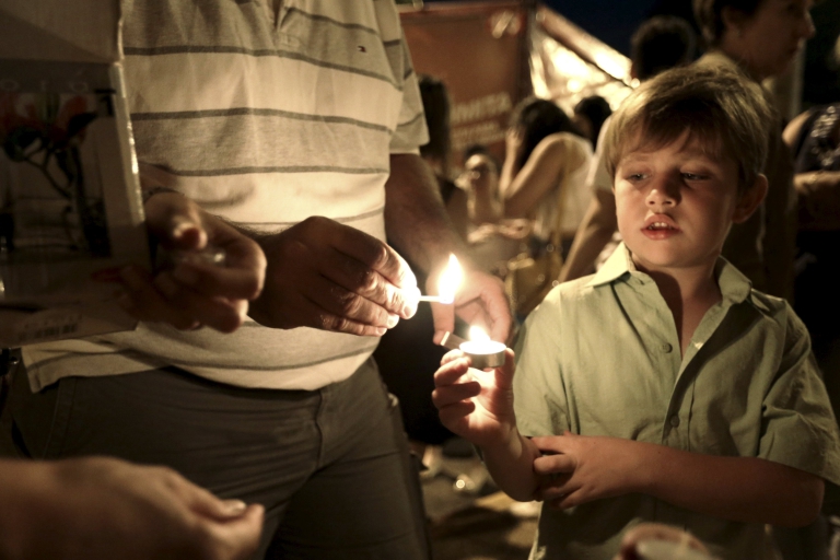 Un niño enciende una vela en la embajada de Francia en Asunción, Paraguay (REUTERS/Jorge Adorno)