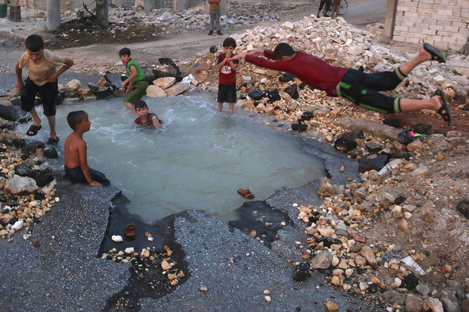 Niños sirios nadan en el cráter dejado por una bomba en Alepo