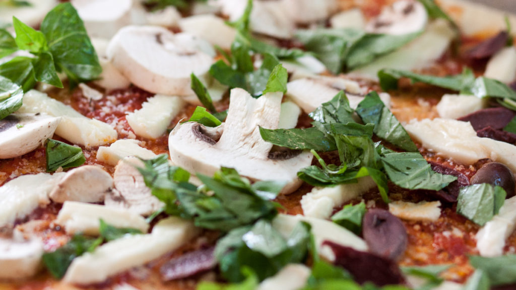 Pizza con ingredientes saludables como champiñones, hojas frescas y pollo.