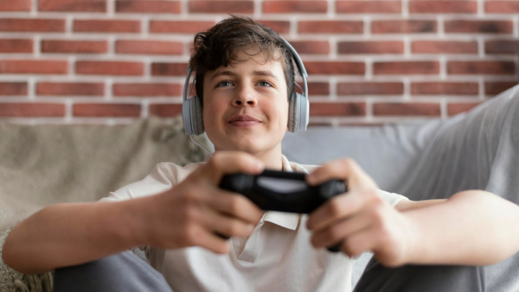 Un adolescente juega a un videojuego con un mando y con auriculares