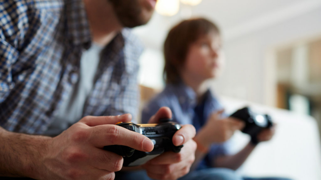 Un padre y un hijo juegan a videojuegos con una consola sentados en el sofá