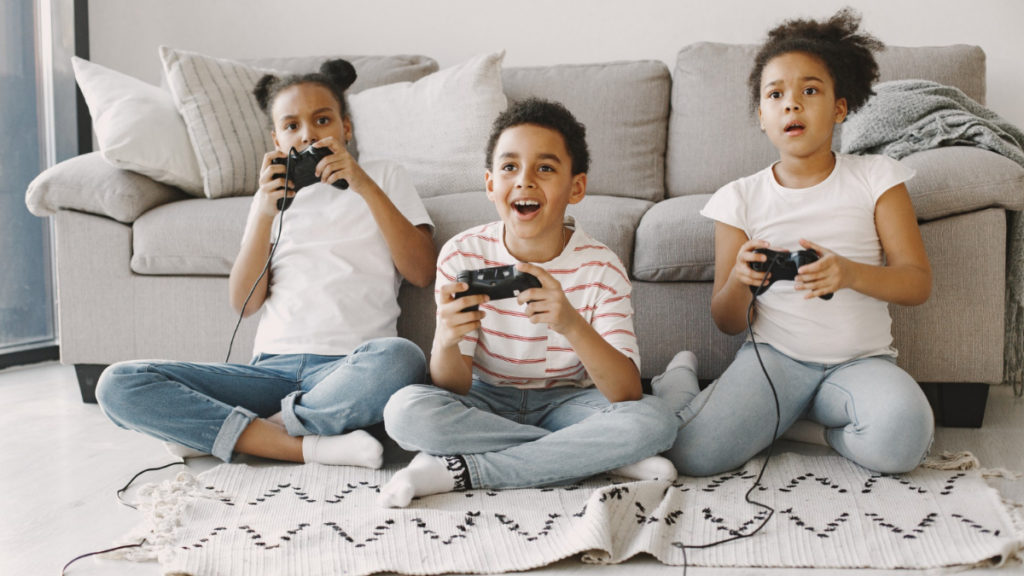 Tres hermanos juegan a videojuegos sentados en el suelo con una videoconsola