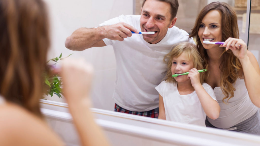 Un hombre, una mujer y una niña se cepillan los dientes frente al espejo.