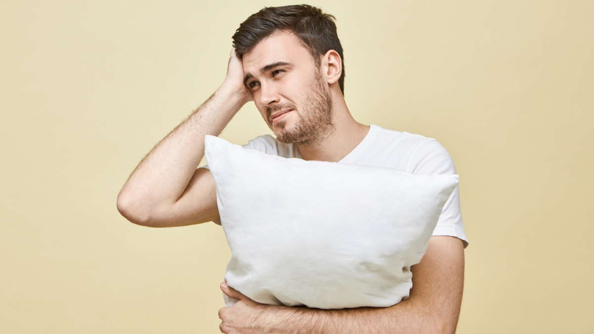 Un hombre agarra una almohada mientras se toca la cabeza 