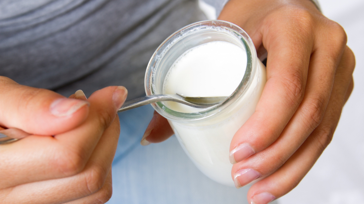 Una mujer sujeta una cucharilla y un yogur en un tarro de cristal alimentos