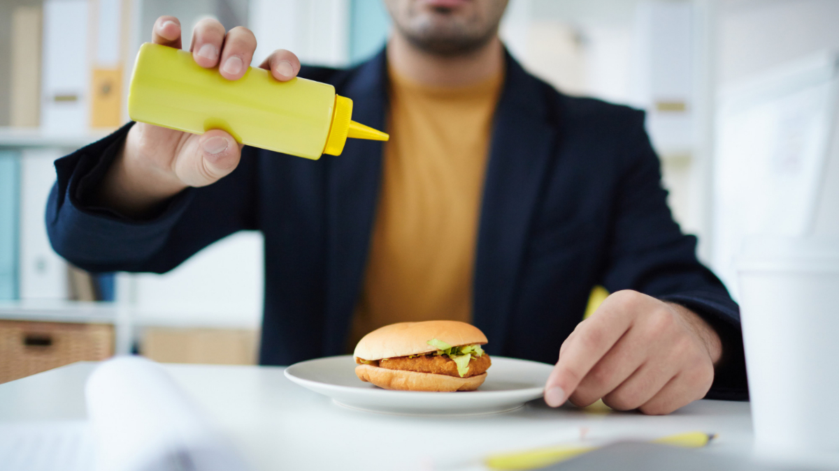 Un hombre añade mostaza a una hamburguesa. 