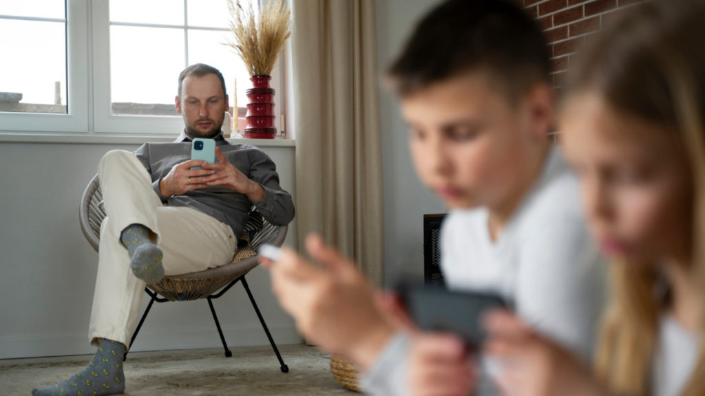 Dos niños tienen un móvil en la mano mientras su padre hace lo mismo