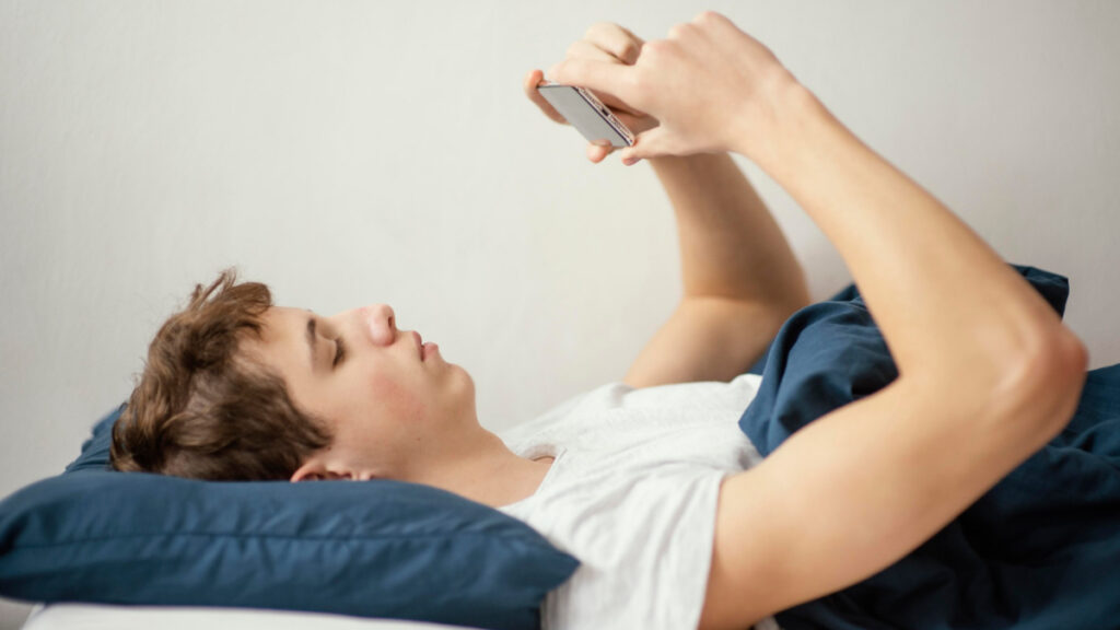 Un adolescente utiliza el teléfono mientras está tumbado en la cama