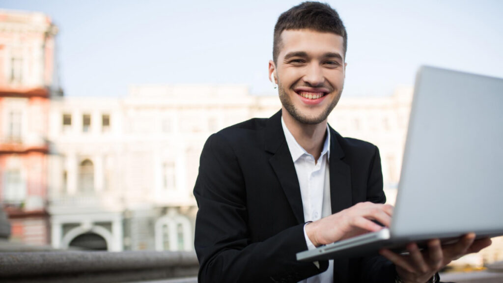 Un hombre sonriente sujeta su ordenador portátil en un espacio público