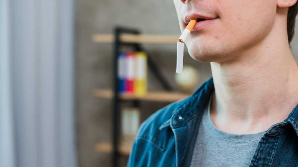 Un hombre sujeta entre los labios un cigarrillo partido.