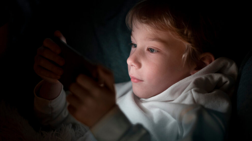 Un niño juega con el teléfono móvil por la noche en la cama.