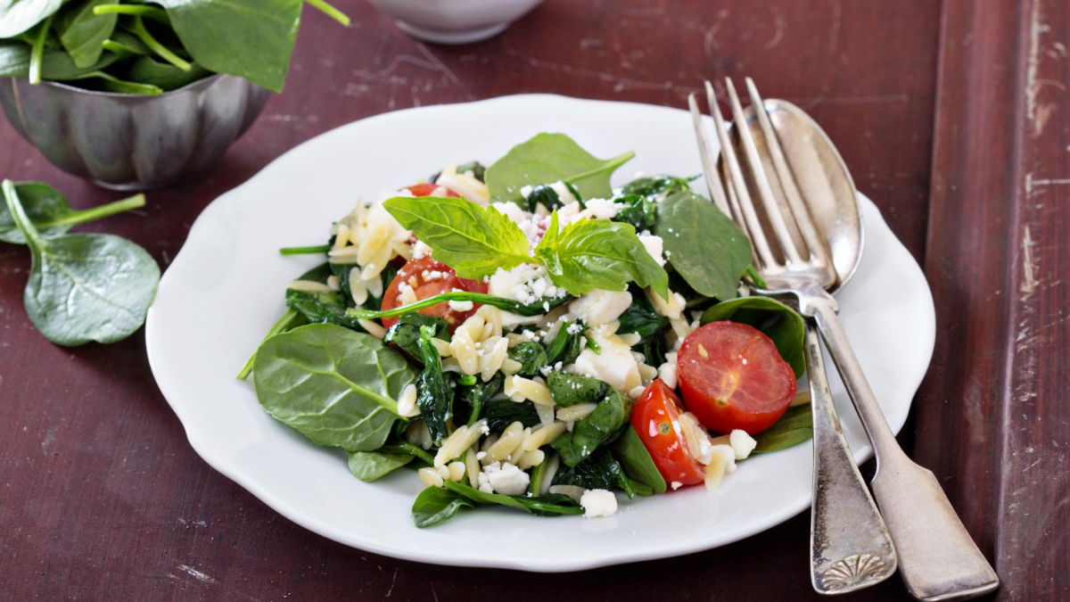 Una ensalada con puntalette, espinacas, queso y tomate