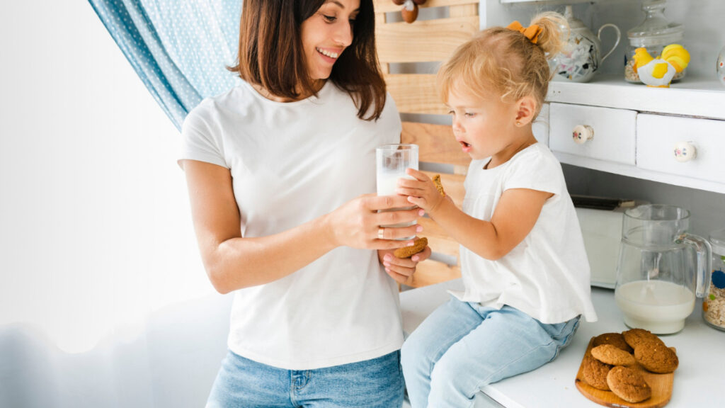 Una madre ofrece un vaso de leche a su hija con unas galletas