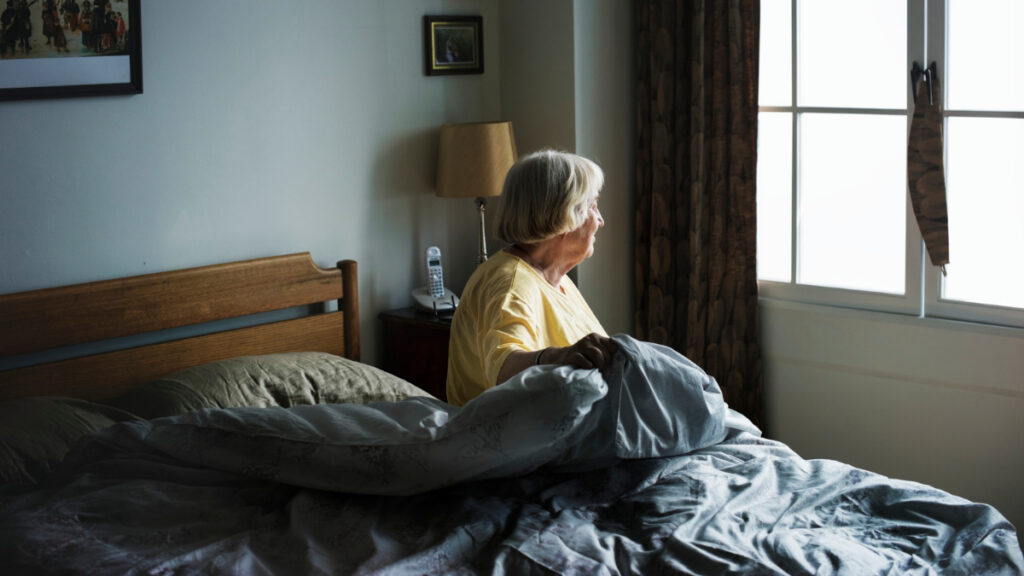 Una mujer mayor con depresión enmascarada mira por la ventana