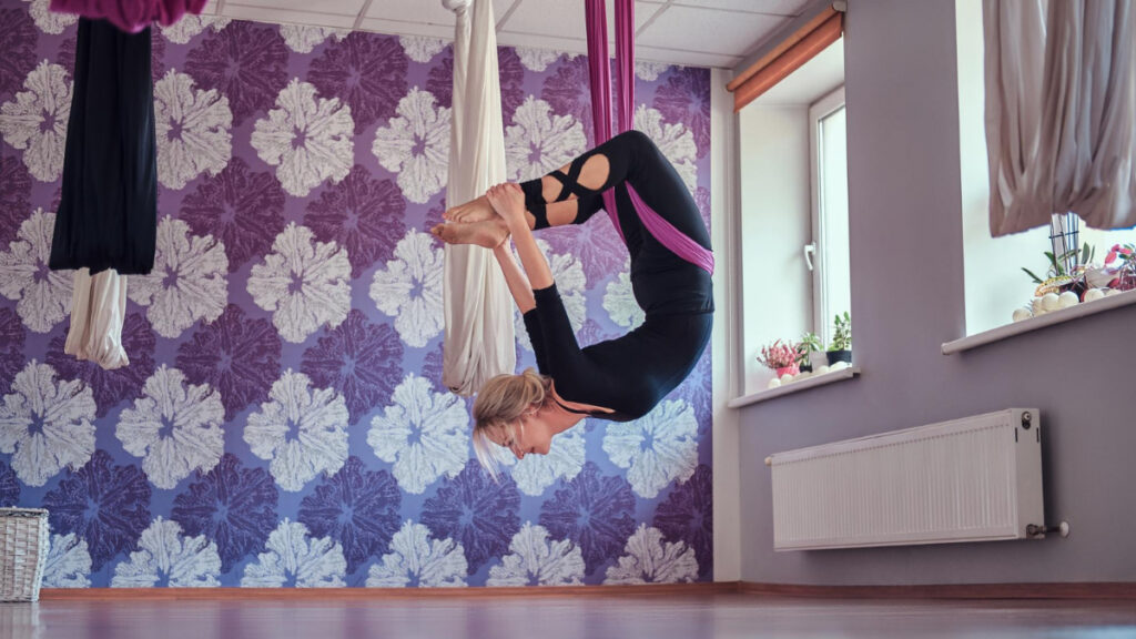 A woman practices aerial yoga at home.