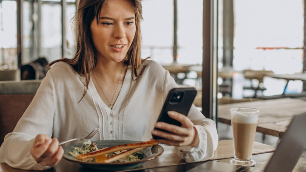 Una mujer se distrae con el teléfono móvil mientras come en su hora de trabajo