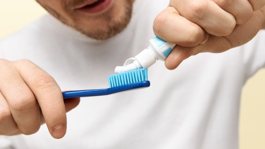 Un hombre joven pone pasta de dientes sobre un cepillo.