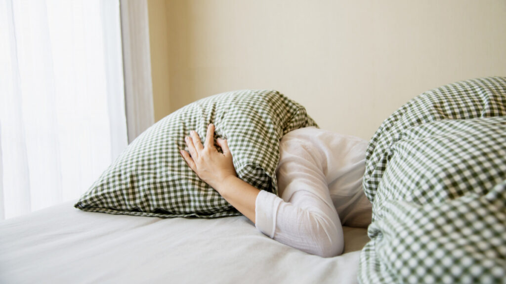 Una mujer se tapa la cabeza con una almohada en la cama