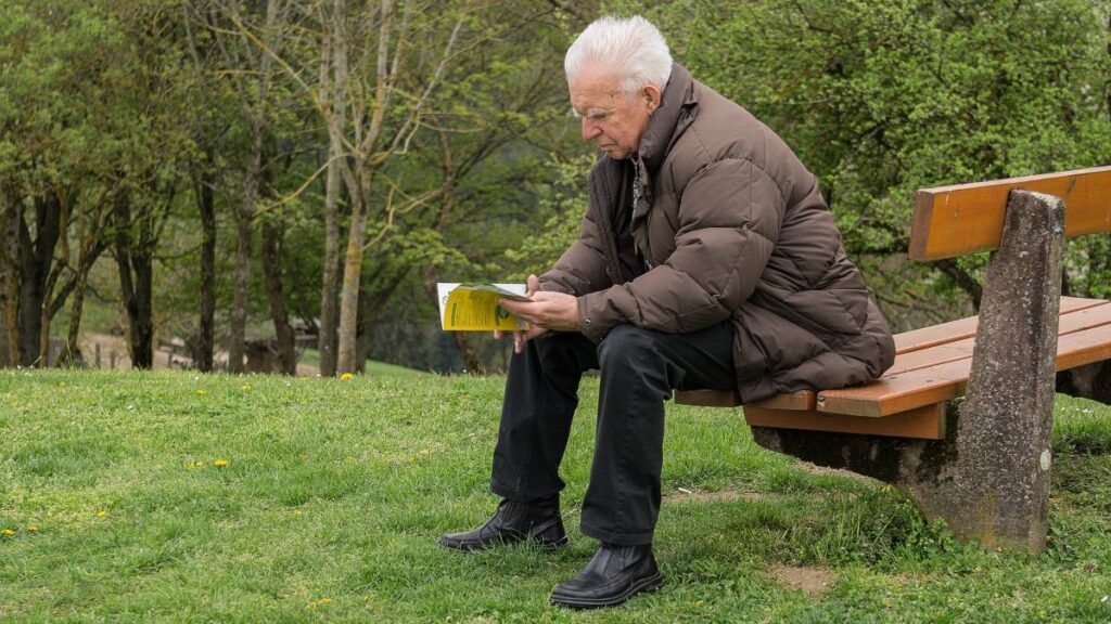 Una persona mayor leyendo en un parque. 