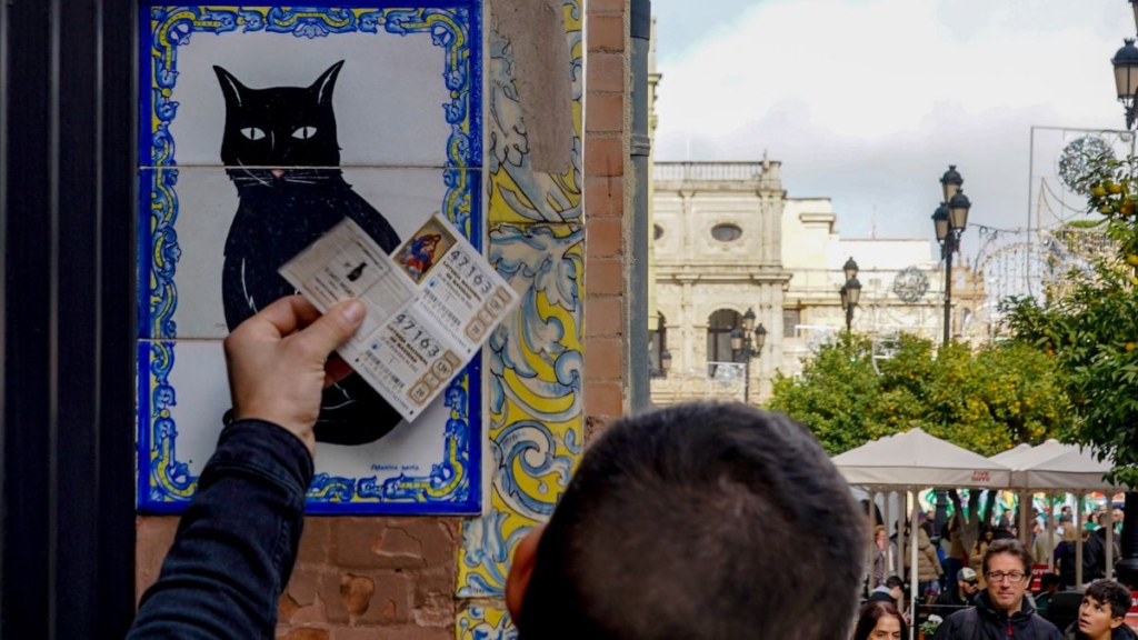 Una persona pone el décimo recién comprado en el azulejo que representa a el gato negro en la administración de loterías ‘El Gato Negro’, en Sevilla. 