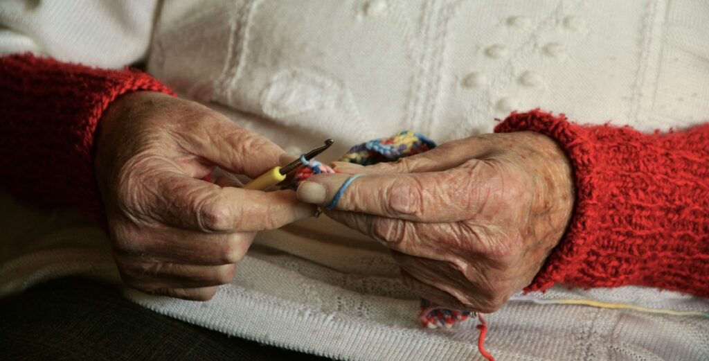 Una mujer mayor haciendo crochet. 