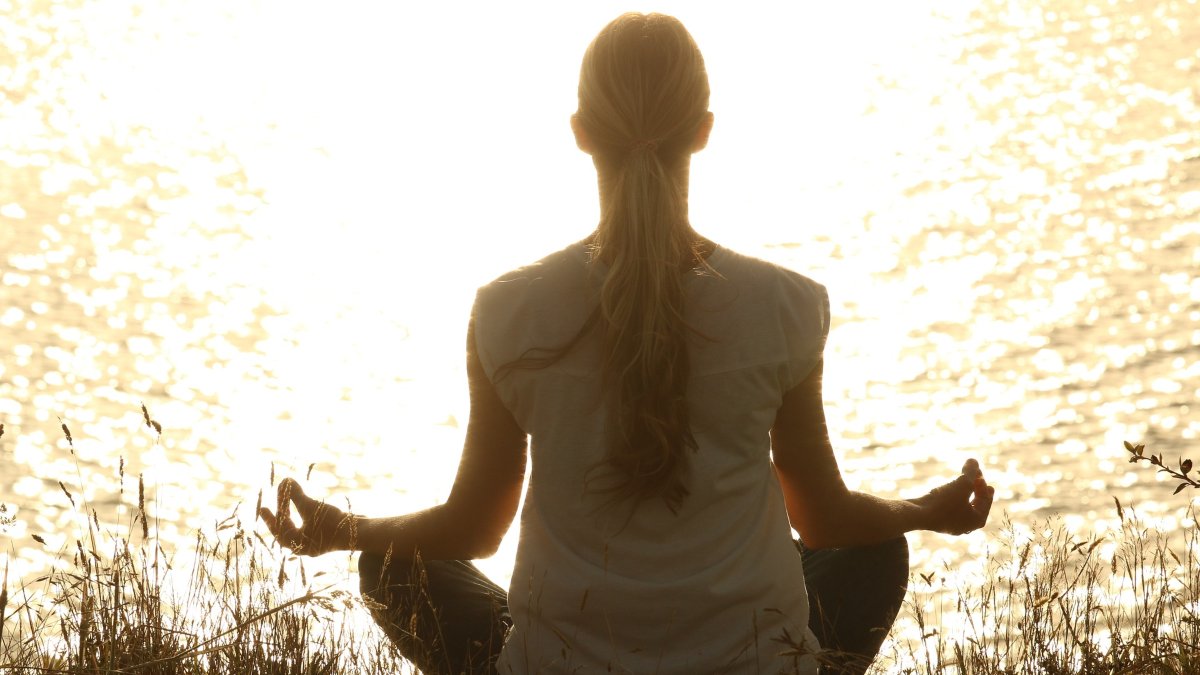 Una mujer meditando frente al agua. 