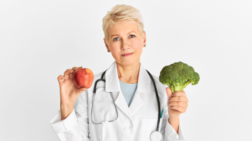 Una doctora sujeta una manzana y un tronco de brócoli