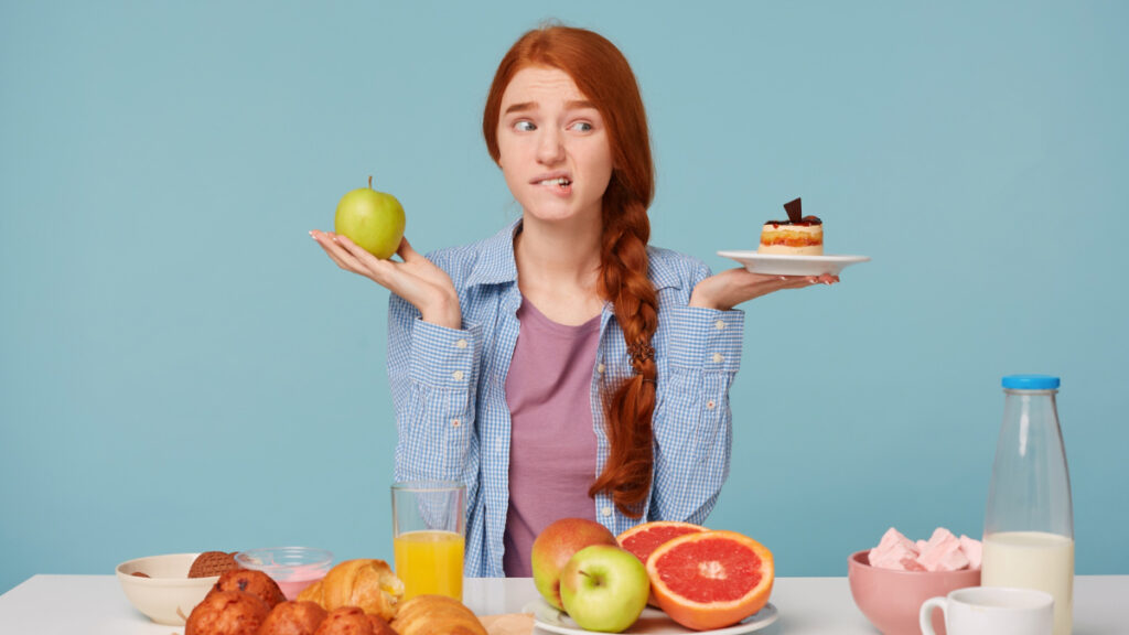 Una mujer ante el dilema del déficit calórico con una manzana y un pastel en cada mano