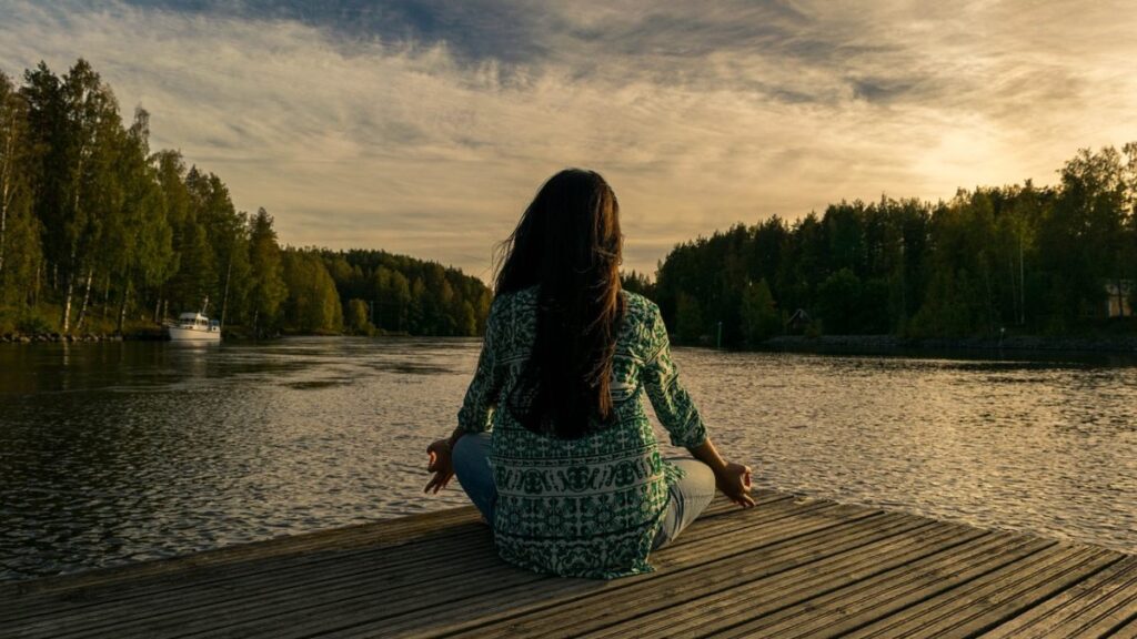 Una mujer meditando frente a un lago. 