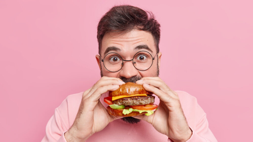 Un hombre empieza a masticar una hamburguesa