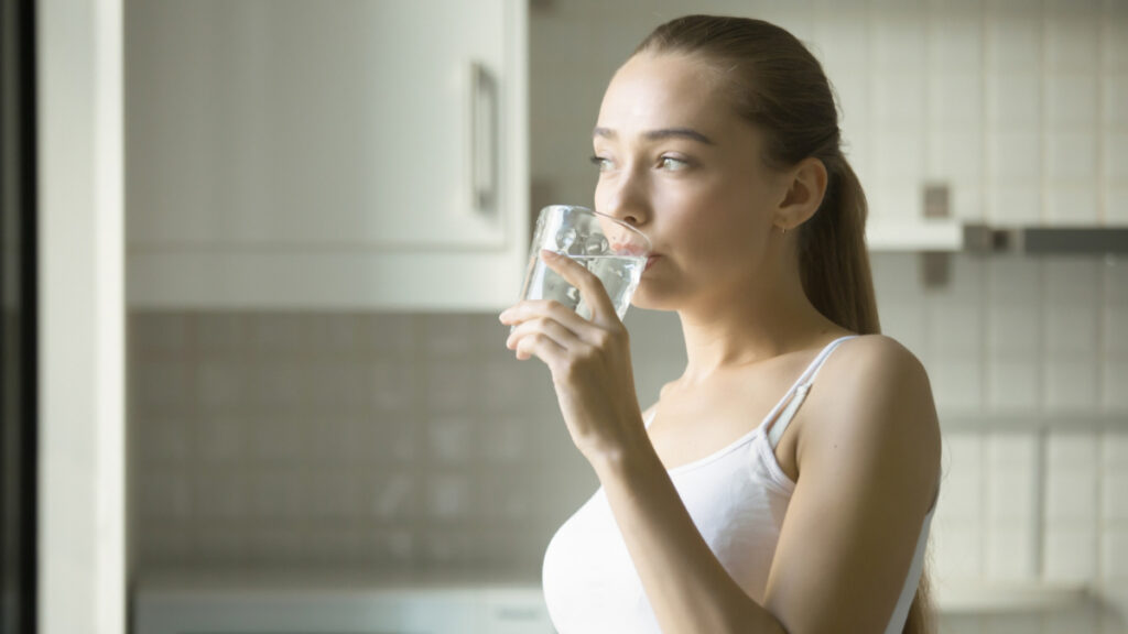 Una mujer bebiendo agua con el riesgo de hiperhidratación
