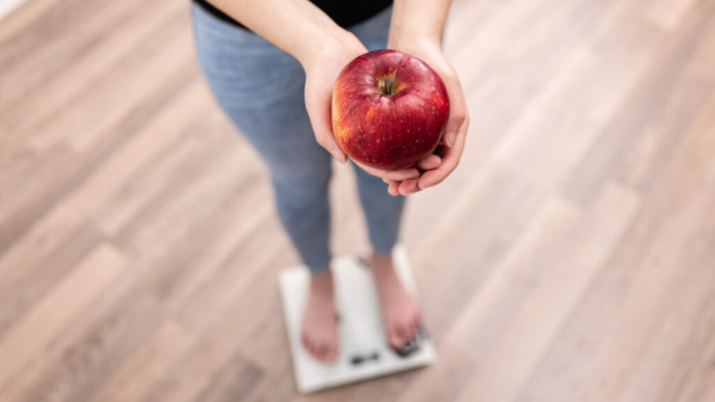 Una mujer subida a una báscula sujeta una manzana