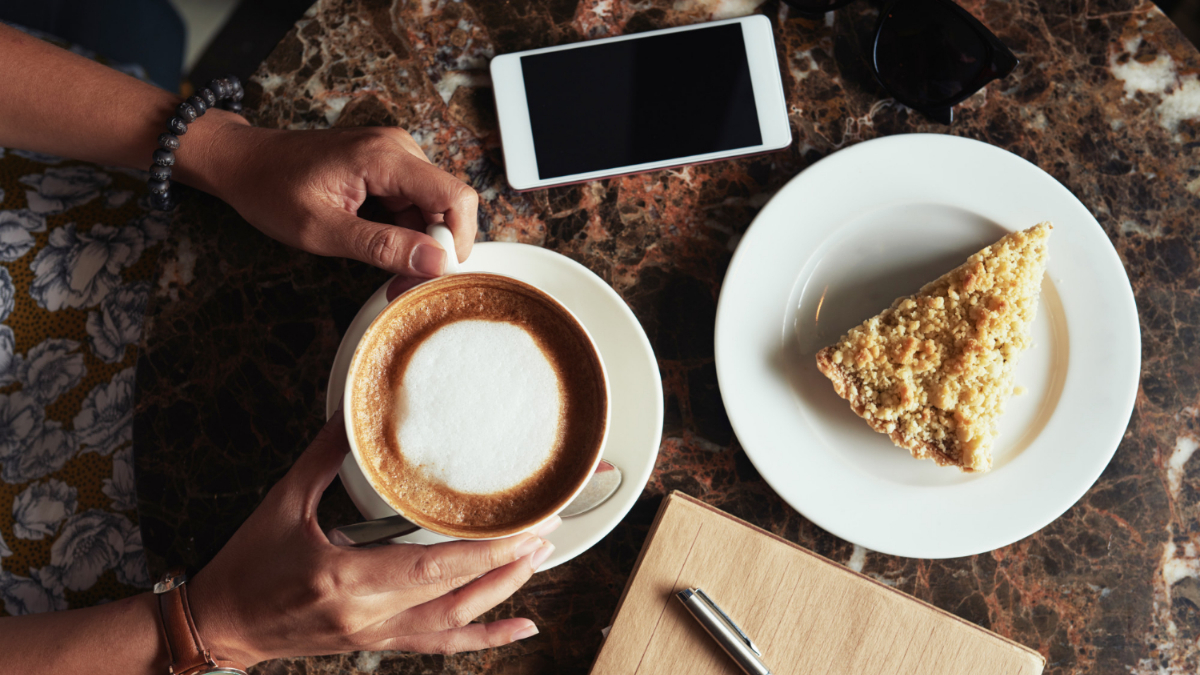 Una mujer sujeta un café con un plato de dulce cerca