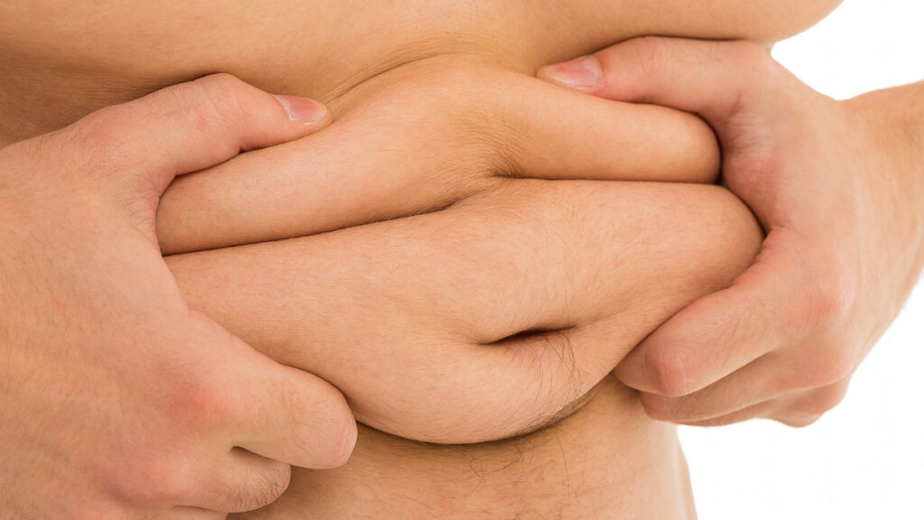 Un hombre con sobrepeso se sujeta la grasa abdominal