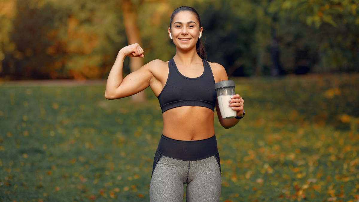 Una chica joven deportista sujeta un batido de proteínas en un parque