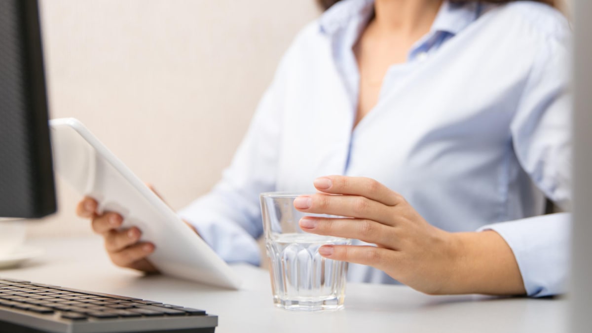 Una mujer sujeta un vaso de agua alcalina en el trabajo