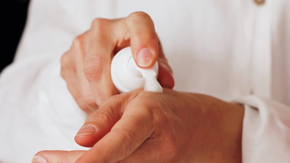 Una persona poniéndose crema en la mano.