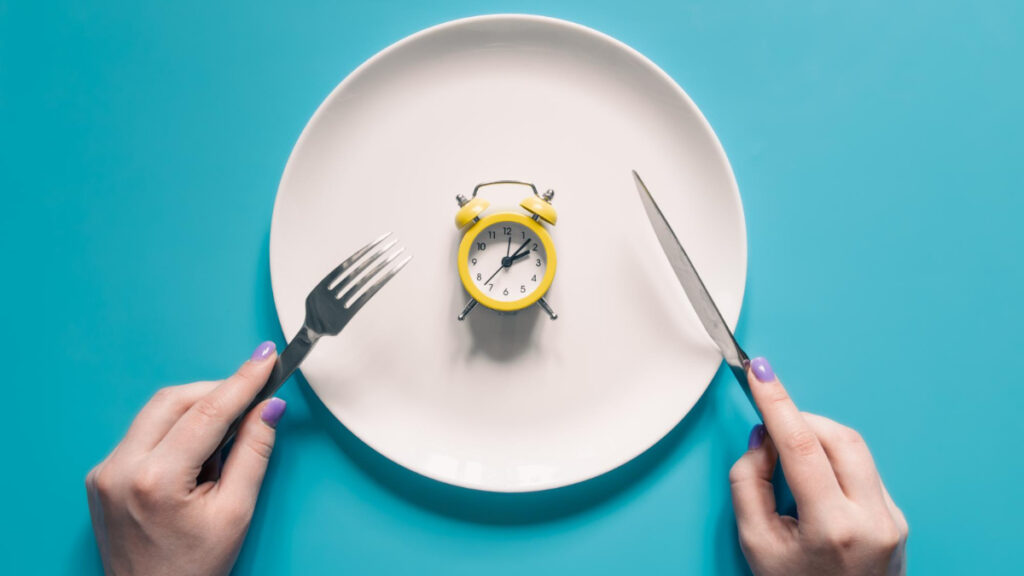Una mujer sujeta unos cubiertos ante un plato con un reloj
