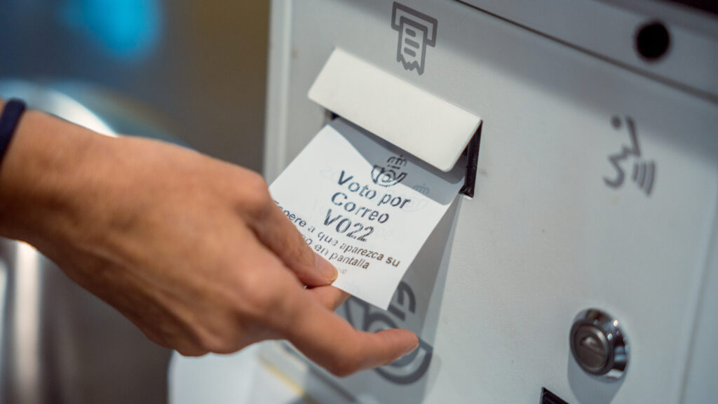 Una persona recoge el ticket para solicitar el voto por correo en el Edificio de Correos.