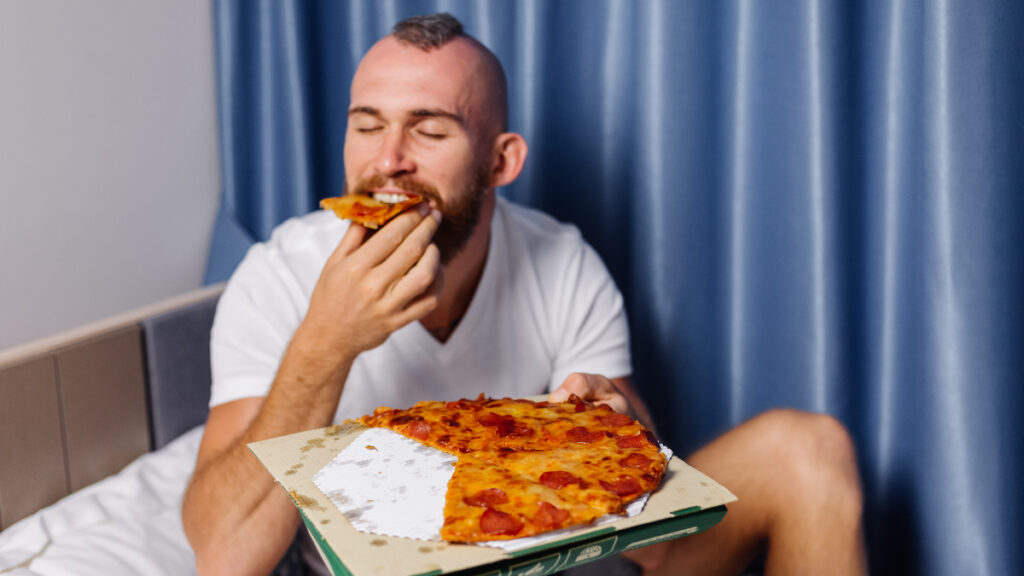 Un hombre come pizza en la cama