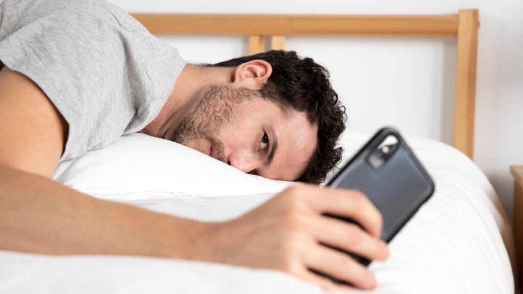 Un hombre mira el móvil en la cama
