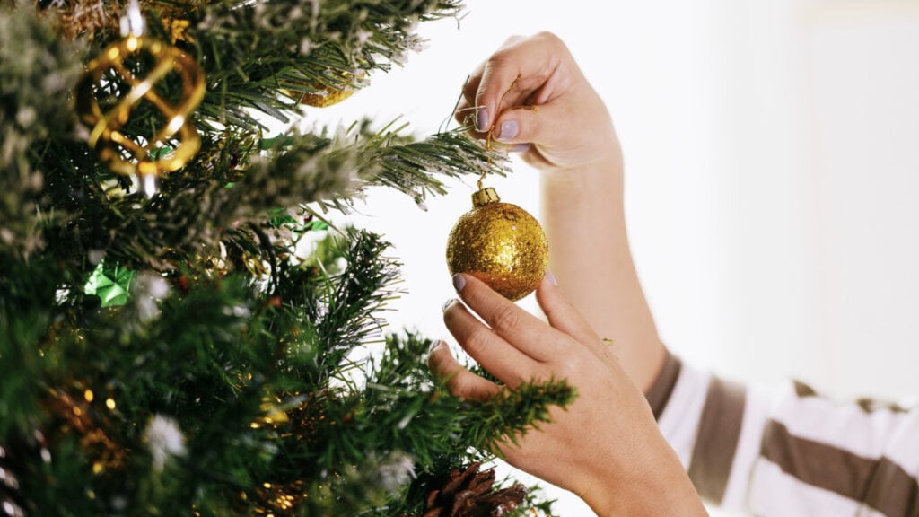 Una persona coloca una bola en un árbol de Navidad