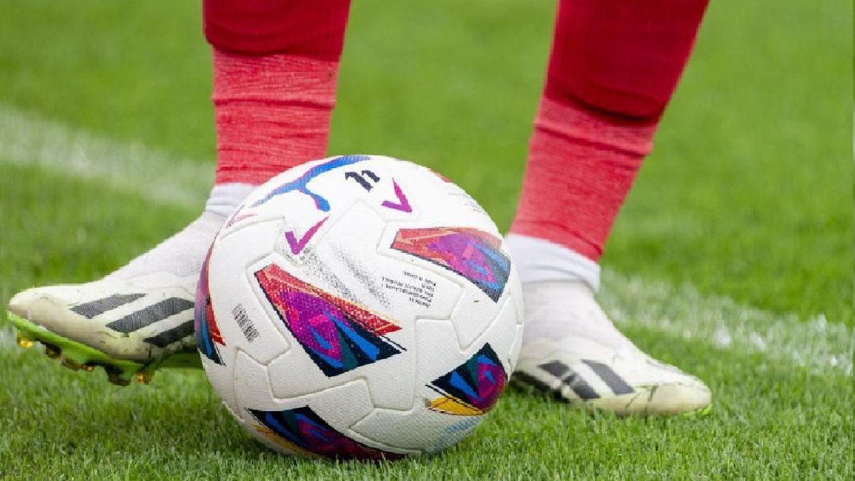 Los pies de un futbolista tocan el balón sobre el césped de un estadio de fútbol.