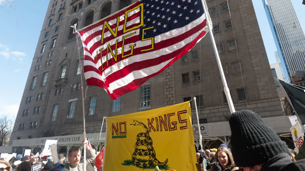 Dos banderas, ambas con el texto "No kings" ("Nada de reyes") sobre sus diseños. La que está arriba es la bandera estadounidense tradicional, 13 barras rojas y blancas y cincuenta estrellas blancas sobre azul. Debajo de ella, la bandera de Gadsden, una bandera con un paño amarillo con una serpiente enroscada sobre sí y un texto que reza "no me pises"