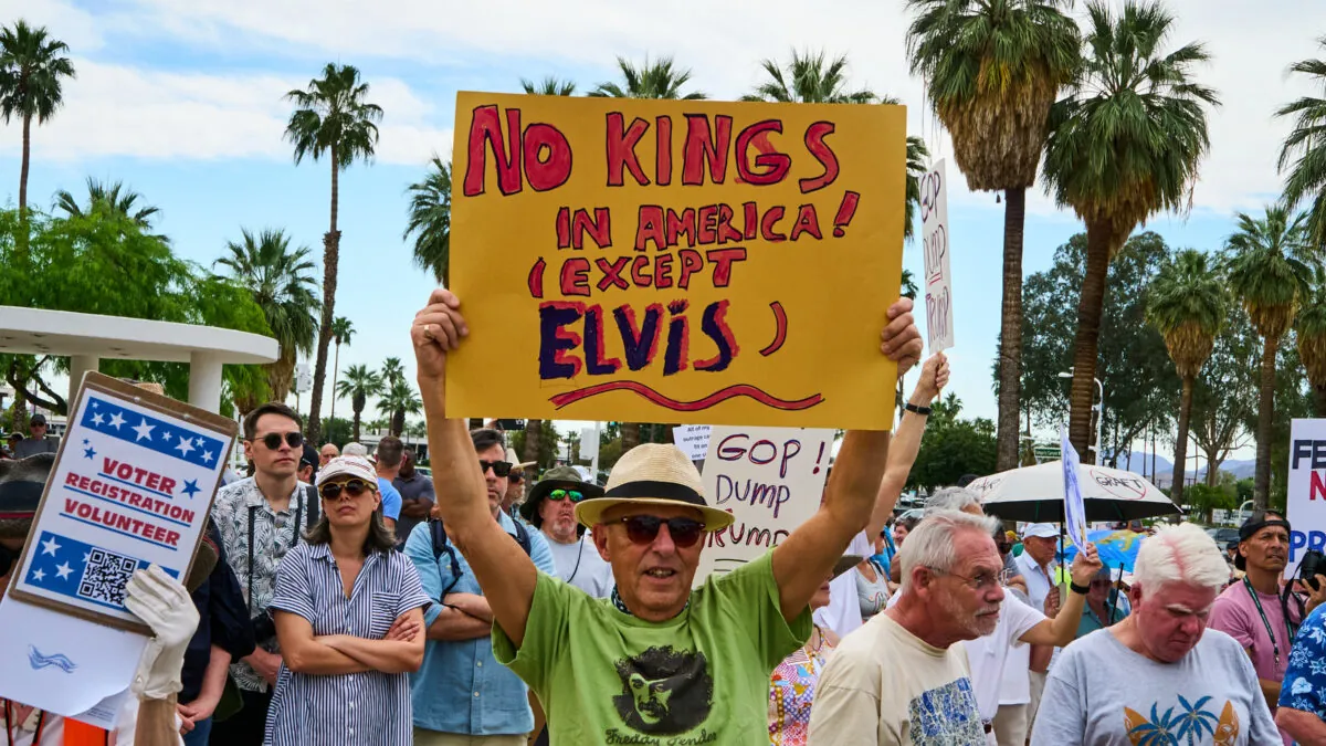 Manifestantes en Palm Springs, California. Hay varias personas. En primer plano, un hombre con sombrero y una camiseta amarilla sostiene una pancarta que reza: "¡En EEUU no hay reyes! (salvo Elvis)"
