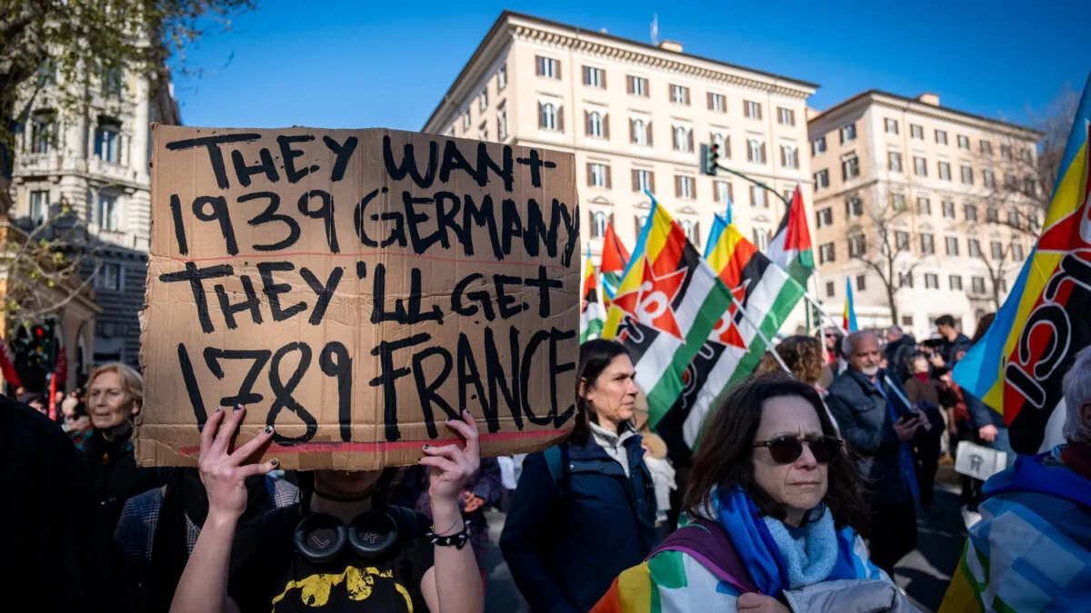 Personas en una plaza en Roma, con varias banderas y tricolores. Una pancarta de cartón reza: "Querían la Alemania de 1939, pero van a tener la Francia de 1789"