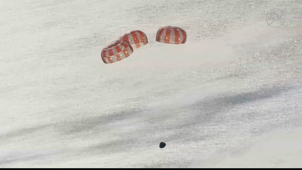 Una cápsula cónica sobre un mar plateado, con tres paracaídas rojiblancos semiesféricos