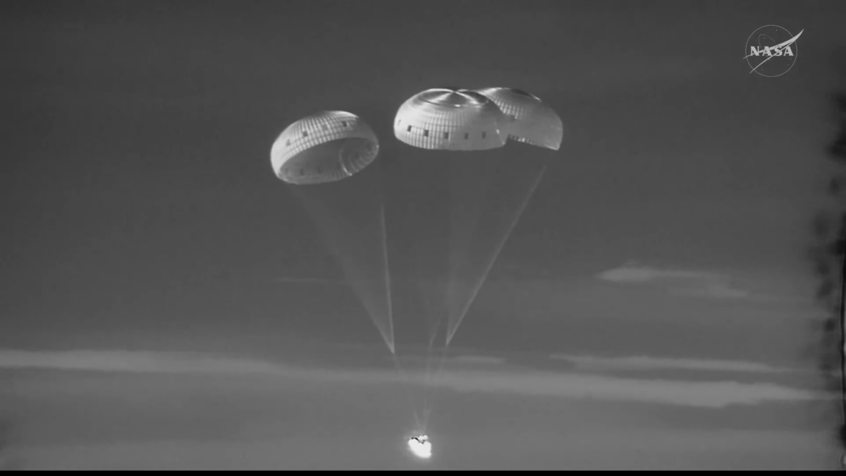 Una imagen infrarroja (en blanco y negro) de una cápsula cónica con tres paracaídas semiesféricos detrás