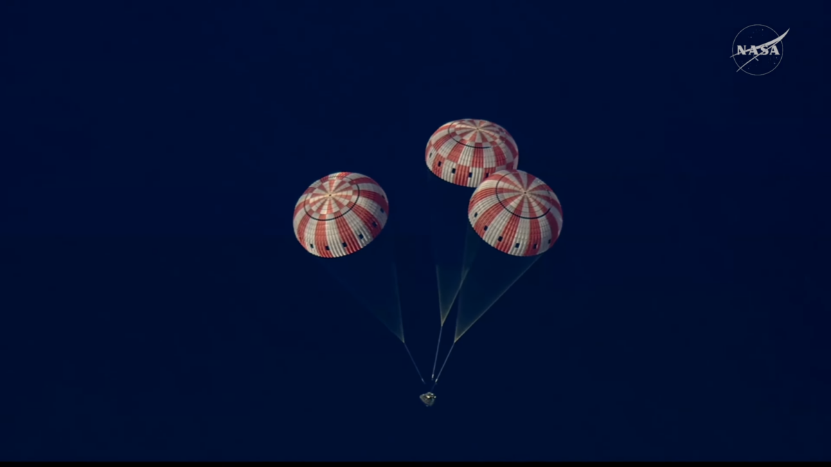 Una cápsula cónica y tres paracaídas rojiblancos semiesféricos sobre un mar de color azul oscuro