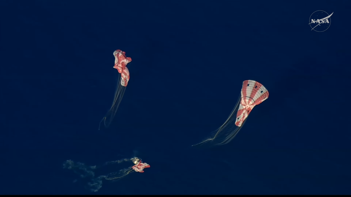 Una cápsula cónica y tres paracaídas rojiblancos desinflándose sobre un mar de color azul oscuro